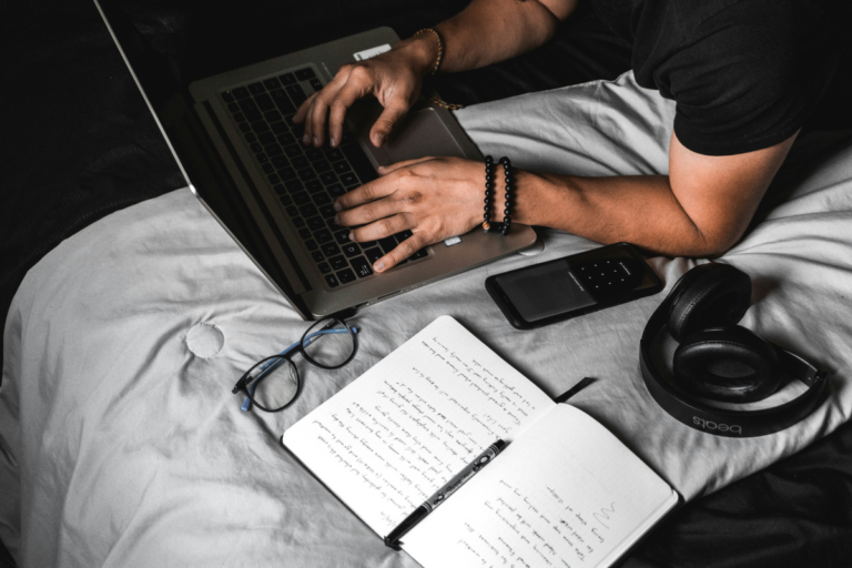 Jovem concentrado estudando em uma mesa organizada com caderno, laptop e fones de ouvido, representando foco e produtividade.
